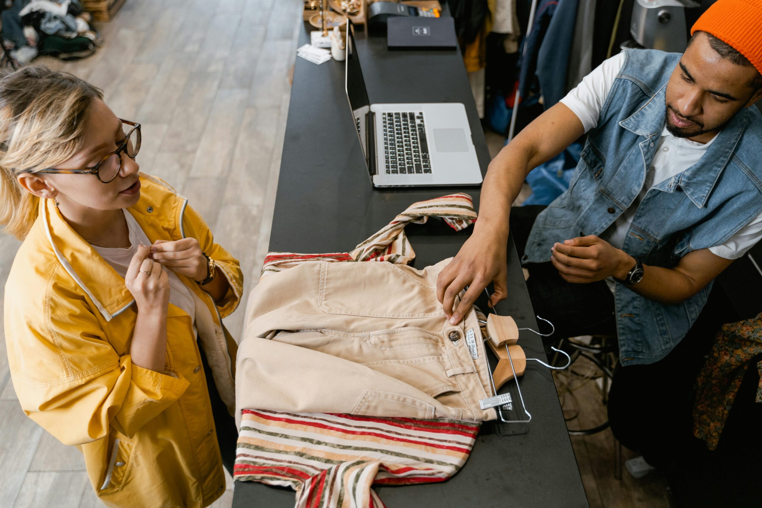 A man and woman at a boutique counter discussing a clothing purchase.